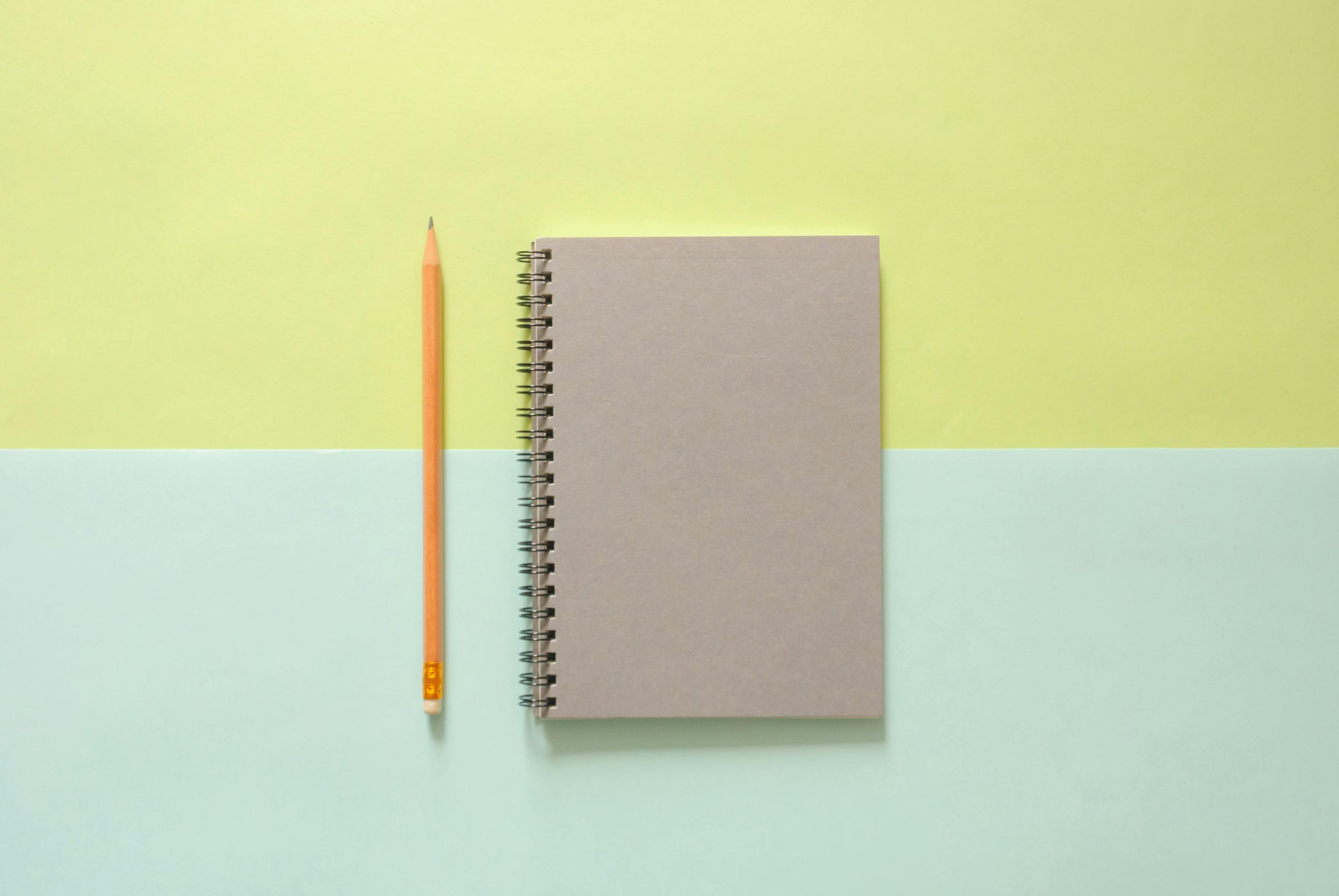 Flat lay of pink polka dot notebook, brown grid notebook, open lined notebook, and pens on a white desk